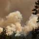 A firefighting helicopter flies past smoke plumes after making a water drop during the Dixie Fire.